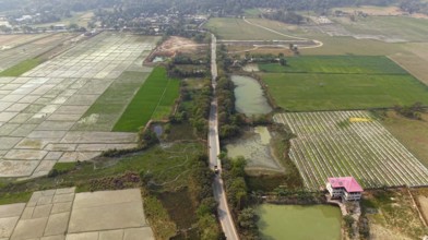 Aerial view of a rural road cutting through patchwork agricultural fields and ponds in the