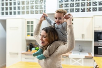 Happy mother giving her cheerful son a piggyback ride at home, celebrating family joy, childhood