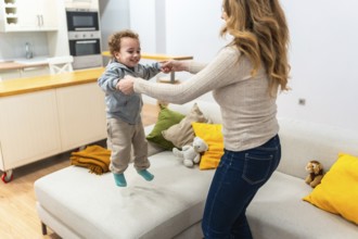 Mother and son holding hands as he joyfully jumps on the living room floor, sharing a bright,