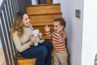 Mother and toddler sitting happily on wooden stairs, engaging in playful interaction with a small
