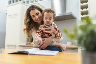Loving mother embracing her happy young son while they are drawing together with colored pencils in