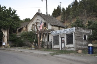 A dilapidated house and a weathered outbuilding surrounded by trees and plants, Mitchell, Oregon,