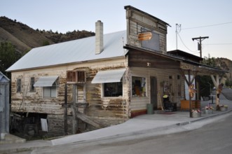 An old, weathered timber house on a hillside with a covered porch and chimney, Mitchell, Oregon,