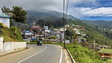 View of a curvy road in a village with hills and green countryside under a cloudy sky, The road on