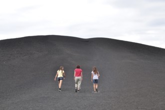 Three people hiking up a trail surrounded by gray lava rock, Craters of the Moon National Monument,