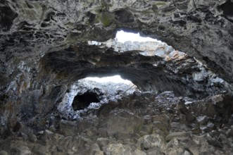 Rocky lava cave opening with irregular walls through which bright light shines in, Craters of the