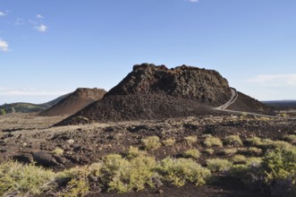 Volcanic cone with lava rock and sparse vegetation crossed by a hiking trail, Craters of the Moon
