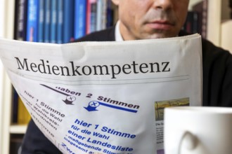Man reads (symbolic) newspaper with the headline MEDIA COMPETENCE