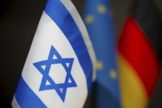 Close-up of the flag of Israel, blurred behind the flags of the EU and Germany