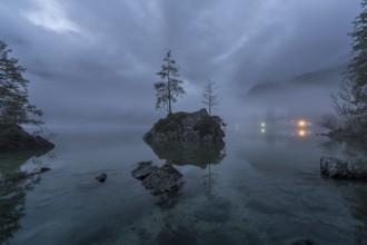 A mystical dawn view of Hintersee Lake in the Bavarian Alps, shrouded in fog with serene, still