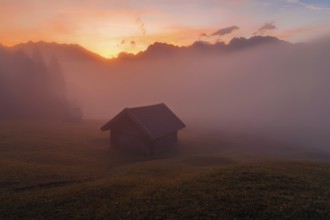 A serene sunrise at Geroldsee in the Bavarian Alps Mist gently envelops wooden huts and grassy