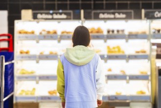 Back view of an unrecognizable woman standing in front of the bakery section in a supermarket,