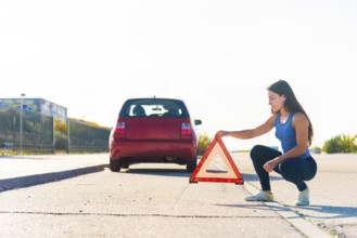 A young woman places a reflective warning triangle behind her car on a roadside This safety
