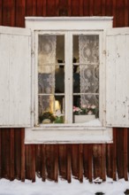 A charming winter scene in Swedish Lapland features a rustic window with lace curtains, revealing a