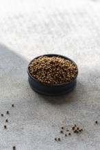 A black bowl filled with coriander seeds rests on a textured concrete surface