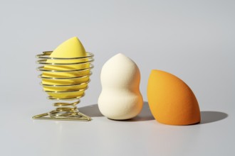 Three cosmetic sponges in vibrant orange and yellow hues, including a unique spiral holder,