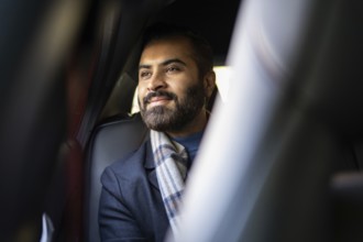 An Indian businessman in a cozy winter outfit looks contemplatively out of a car window, showcasing