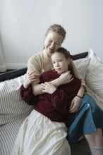 A tender moment of a mother and daughter sharing an embrace while seated on a cozy couch, capturing