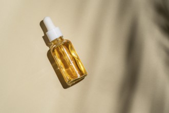 Top view of a transparent glass dropper bottle with golden liquid is angled on a beige background,