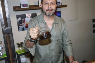 A barista in a cozy cafe confidently showcases a pot of freshly prepared specialty coffee