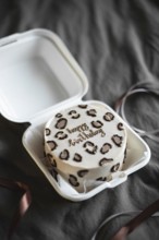 Stylish bento birthday cake with leopard print and golden lettering, neatly presented in a white