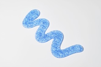 A blue face scrub with micro-exfoliating particles is arranged in a wave pattern on a white surface