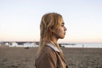 Mixed-race woman with blonde hair in profile, gazing at the sea She stands on a sandy beach during
