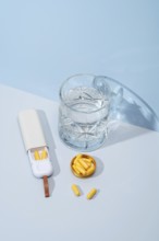 Top view of a white pillbox with orange capsules, a crystal glass filled with water, and extra