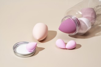 A collection of pink and beige cosmetic sponges arranged on a neutral beige background, ideal for
