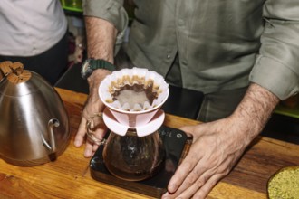 A barista skillfully prepares specialty coffee using a pour-over method. The setup includes a