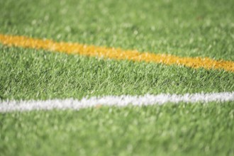 A detailed close-up of green artificial turf with bold white and yellow lines, capturing the