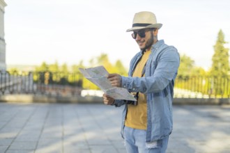 A Latino transgender man, wearing casual denim and a straw hat, navigates a city with a map in hand