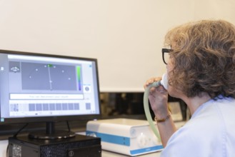 A middle-aged woman undergoing a spirometry test in a pneumology department, displaying her breath