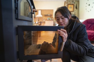 An Asian female looks down while meticulously cleaning the glass door of a wood burning stove in a