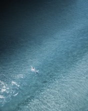 An aerial shot of a lone surfer paddling through calm turquoise waters along the Portuguese coast.