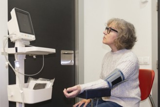 A mature woman undergoes a blood pressure test in a modern clinic, sitting calmly with a monitor