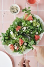 Top view of cropped unrecognizable hands eating vibrant salad featuring ruccola, watermelon,