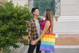 A loving lesbian couple shares a warm embrace while holding hands in an urban setting. One partner