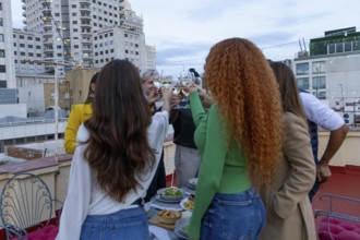 A lively group of friends celebrates on a rooftop, raising glasses in a toast Surrounded by city