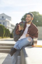 Latino transgender man sitting outdoors, smiling and using a smartphone on a sunny day He's