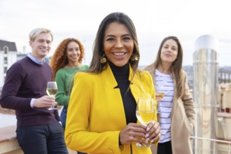 A group of cheerful friends enjoying a casual gathering on a rooftop, holding glasses of wine The