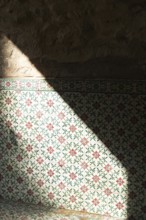 Sunlight splits across a wall covered in traditional Moroccan ceramic tiles, casting shadows and