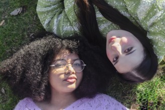 Two friends relax on grass, enjoying the sunshine. One wears glasses and has curly hair, the other