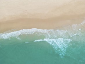 A breathtaking aerial photograph of a sandy beach in Portugal, where gentle turquoise waves meet