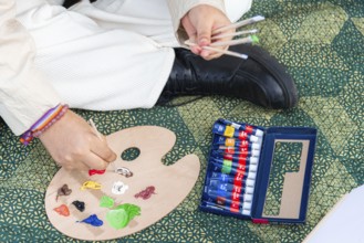 A close up of a young black woman preparing a wooden palette with colorful paint tubes and brushes
