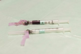 A close-up image of medical syringes filled with blood, laid on a sterile aqua-colored surface,