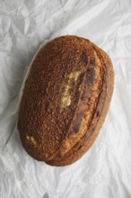 Top view of a freshly baked sourdough bread with a crusty top, resting on crumpled white paper