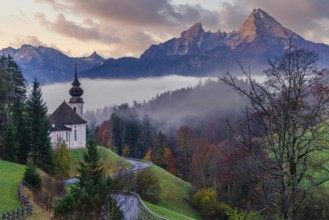 The picturesque Maria Gern Church is nestled among vibrant autumn foliage with the majestic