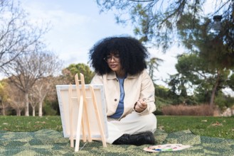 Young black woman with curly hair immersed in painting outdoors, capturing a scenic day in nature.