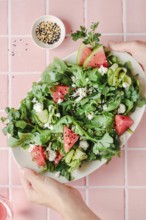 Top view of cropped unrecognizable hands with colorful arugula, watermelon, cucumber, and feta